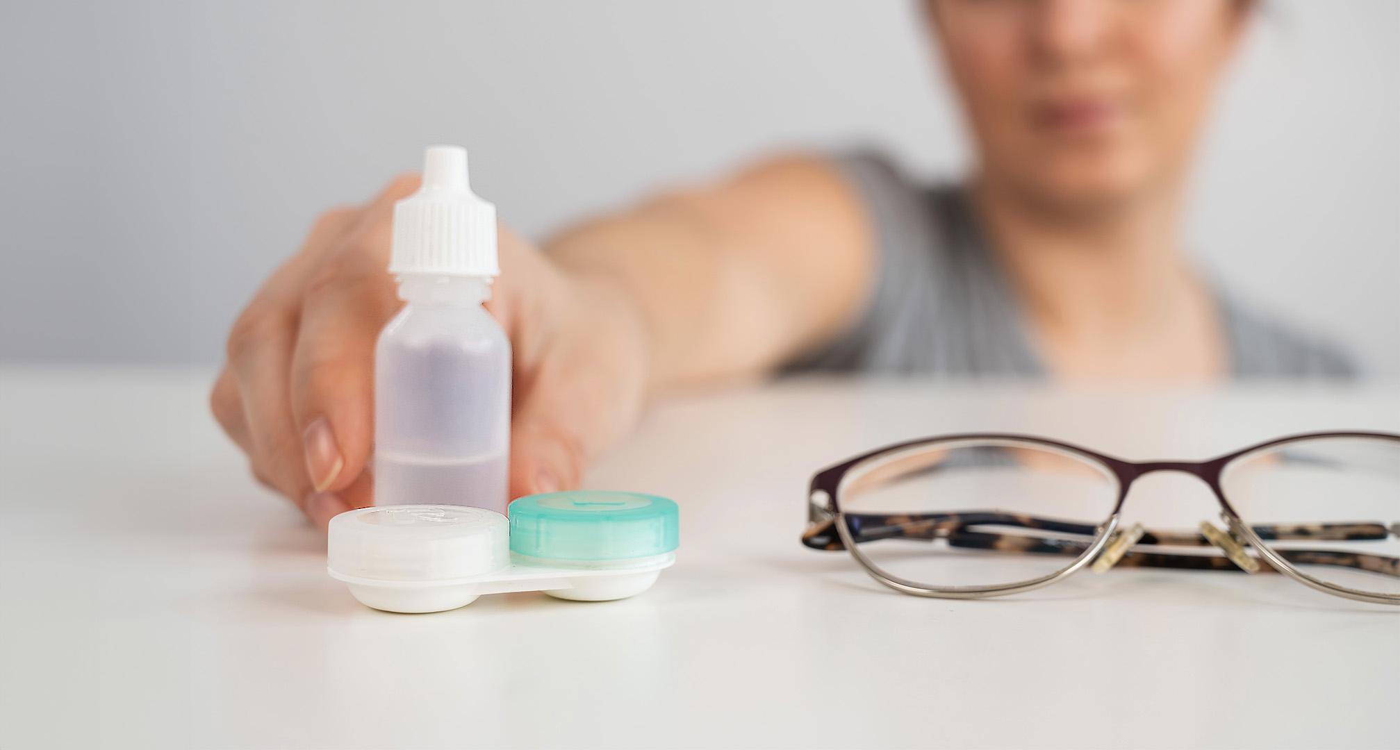 Nahaufnahme von Augentropfen, Kontaktlinsenbehälter und Brille auf weißem Tisch